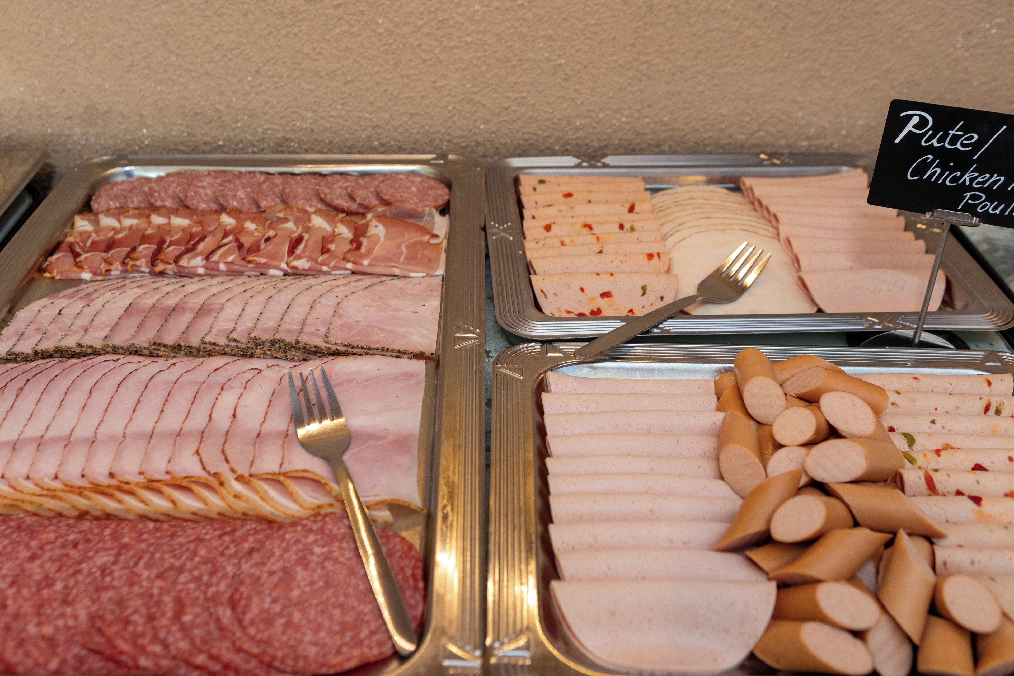 A buffet with various meats including sliced ham, sausages, and chicken.