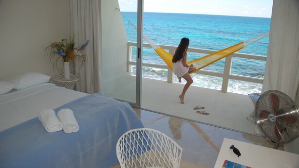 A room with a bed, a chair, a fan, and a view of the ocean.
