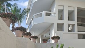 A modern multi-story building with balconies, potted plants, and a stone wall.