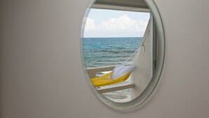 A circular window with a hammock and a pillow, overlooking the ocean.
