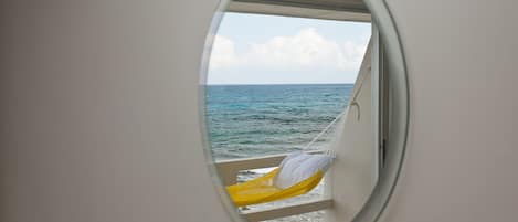 Una ventana circular con una hamaca y una almohada, con vista al océano.