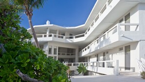 A modern multi-story building with balconies, surrounded by lush greenery and palm trees.