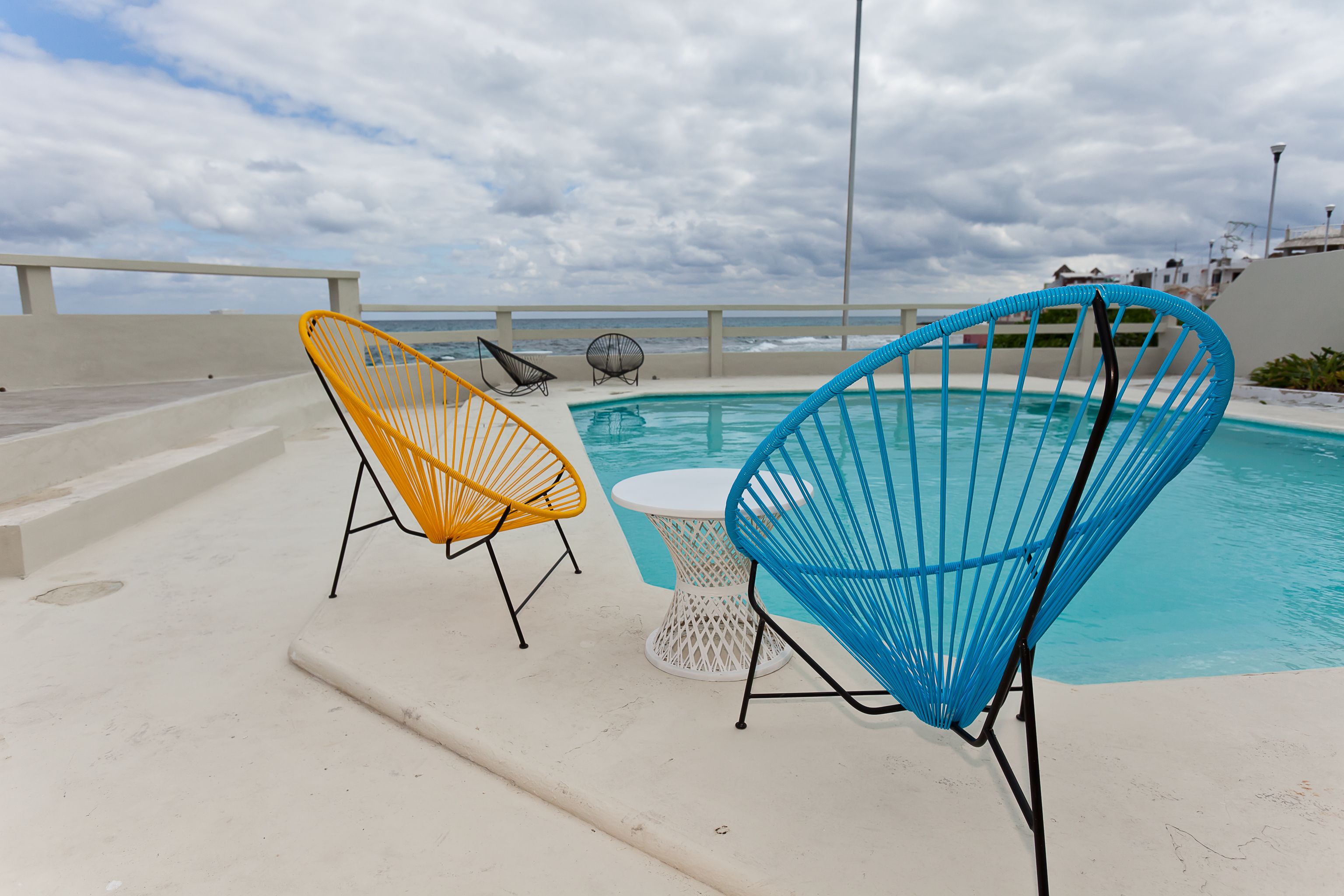 Un espace aménagé au bord de la piscine, avec deux chaises et une table, offrant une vue sur l’océan.