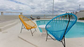 A poolside area with two chairs and a table, overlooking the ocean.
