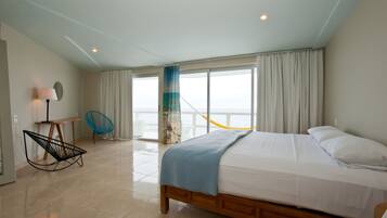 Un dormitorio con una cama grande, una silla, un escritorio y vistas al mar a través de un ventanal corredero.