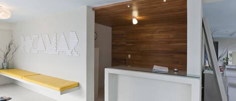 A reception area with a wooden panel wall, a glass-top reception desk, and a yellow bench.