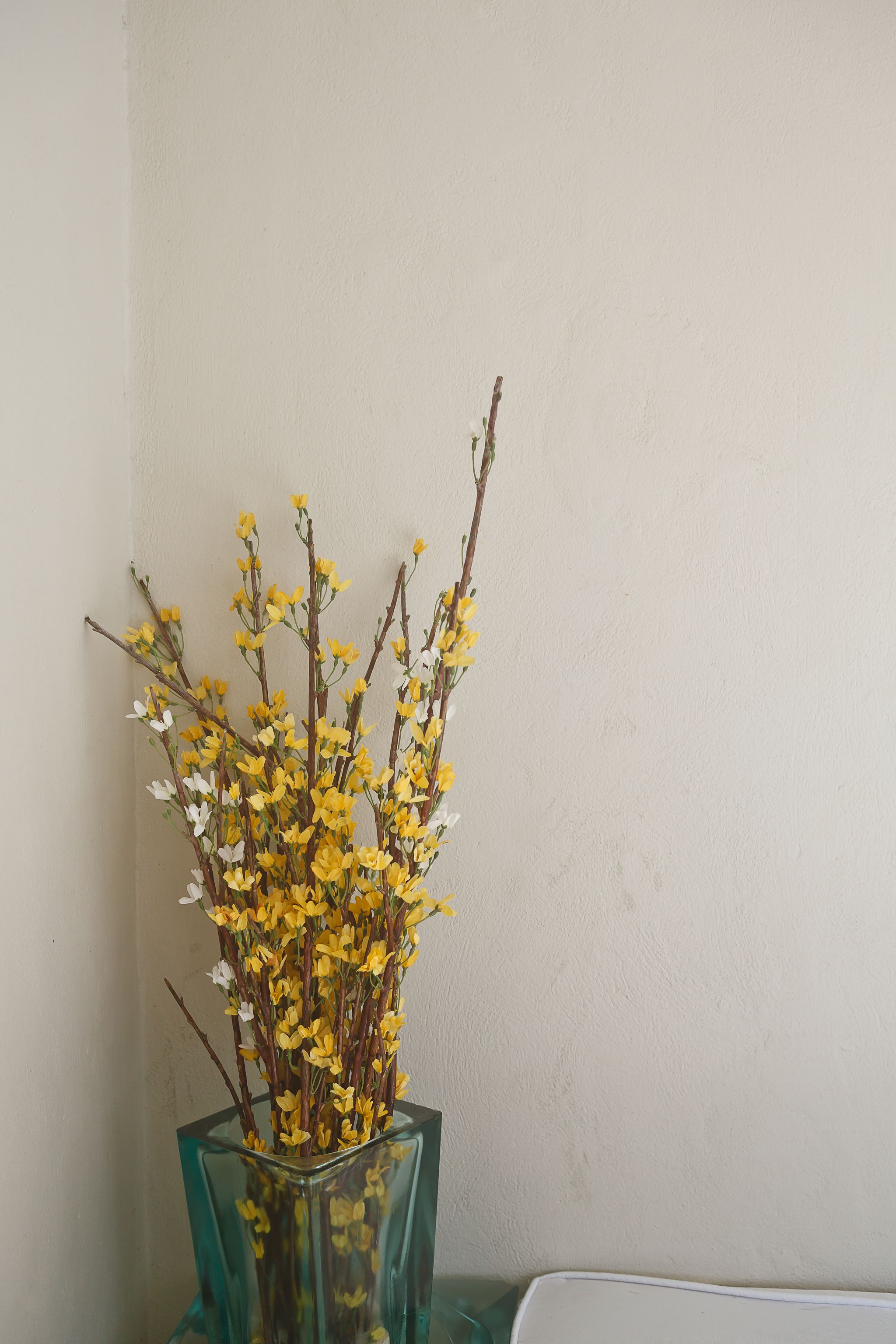 A clear glass vase with yellow flowers against a plain wall.