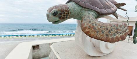 A sea turtle statue on a pedestal by the ocean.