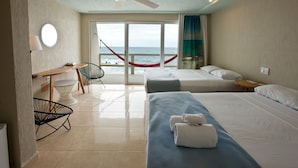 A hotel room with two beds, a desk, a chair, a hammock, and a view of the ocean.
