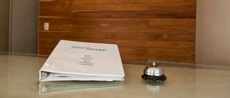 A hotel brochure titled "Hotel Rocamar" on a glass table with a wooden wall background.