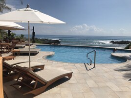 Zona de piscina con sillones de descanso y sombrillas, con vistas al océano.