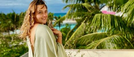 A person sitting on a balcony with a view of palm trees and a body of water.