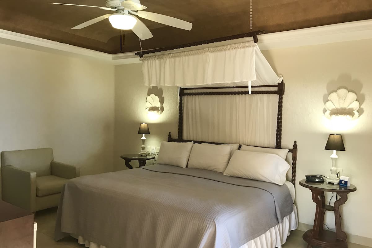 A bedroom with a four-poster bed, a ceiling fan, and two bedside lamps.