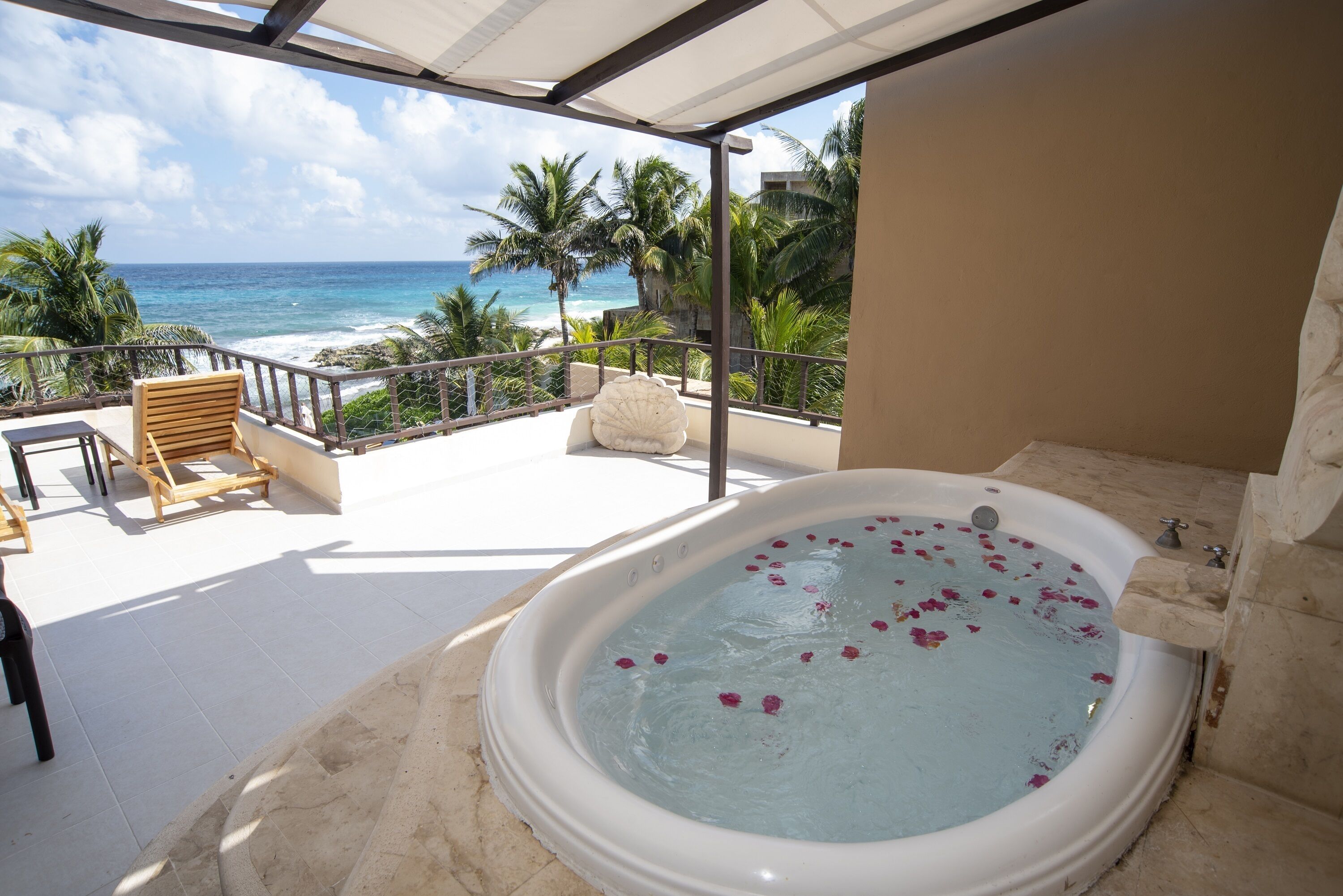 Un balcon avec un jacuzzi, des chaises en bois et une vue sur l’océan.