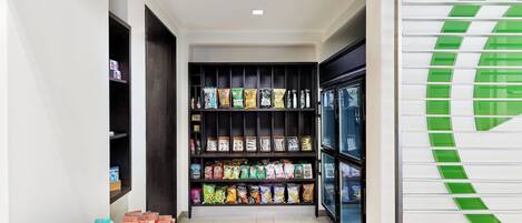 A corridor with shelves stocked with snacks and beverages, leading to a door with a green logo.