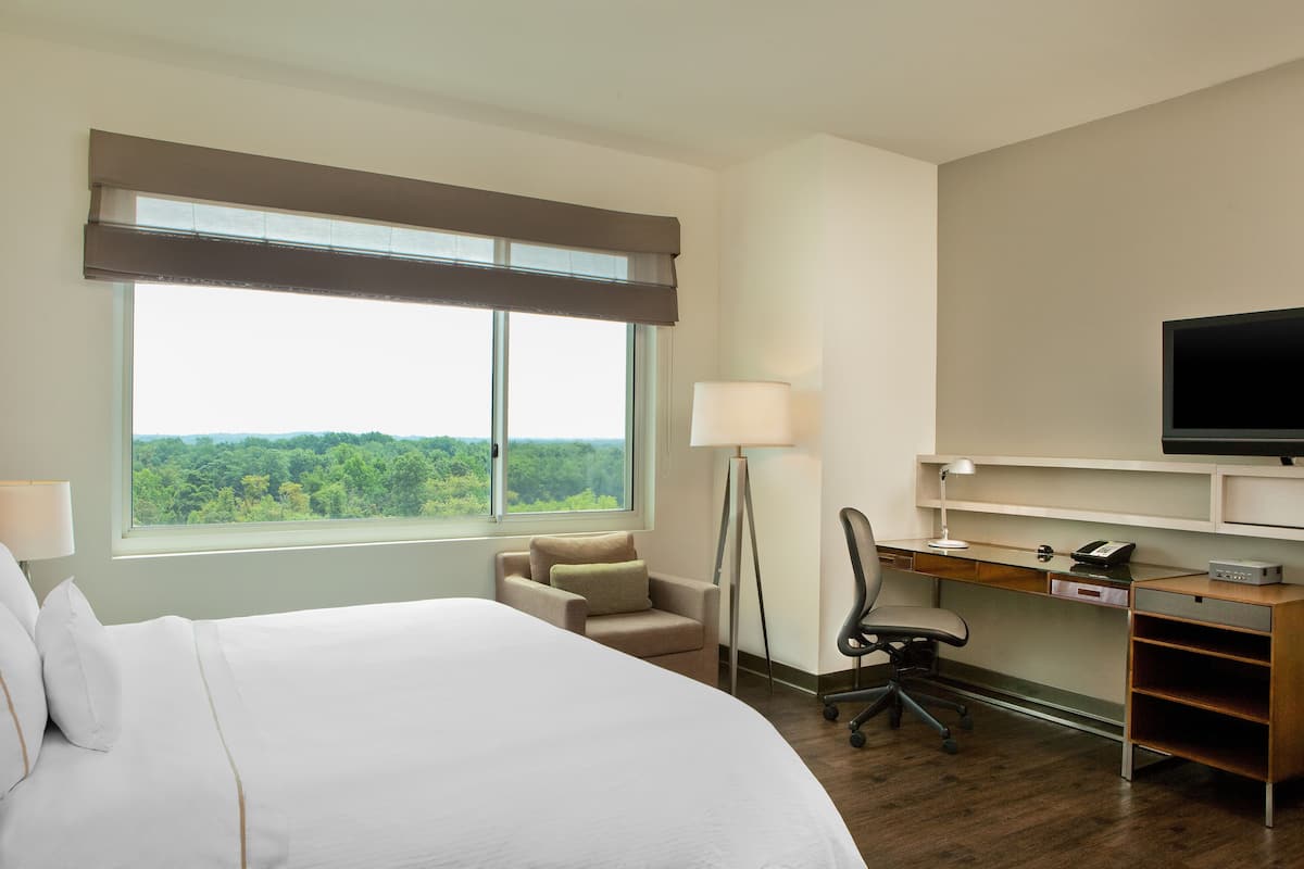 A hotel room with a large bed, a desk with a computer, a chair, a lamp, and a TV.
