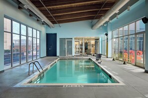 Una piscina interior con paredes de vidrio transparente, techo de madera y vistas al exterior.