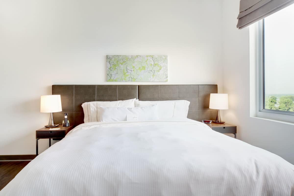 A hotel room with a large bed, two bedside tables with lamps, a headboard, and a window with a view.