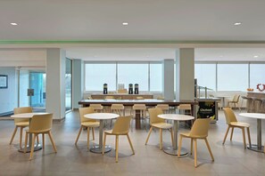 A spacious indoor area with multiple tables and chairs, large windows, and a counter with a sign. - Element by Marriott Arundel Mills BWI Airport (Hanover)