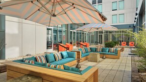 An outdoor seating area with cushioned sofas, striped umbrellas, and a modern building in the background. - Element by Marriott Arundel Mills BWI Airport (Hanover)