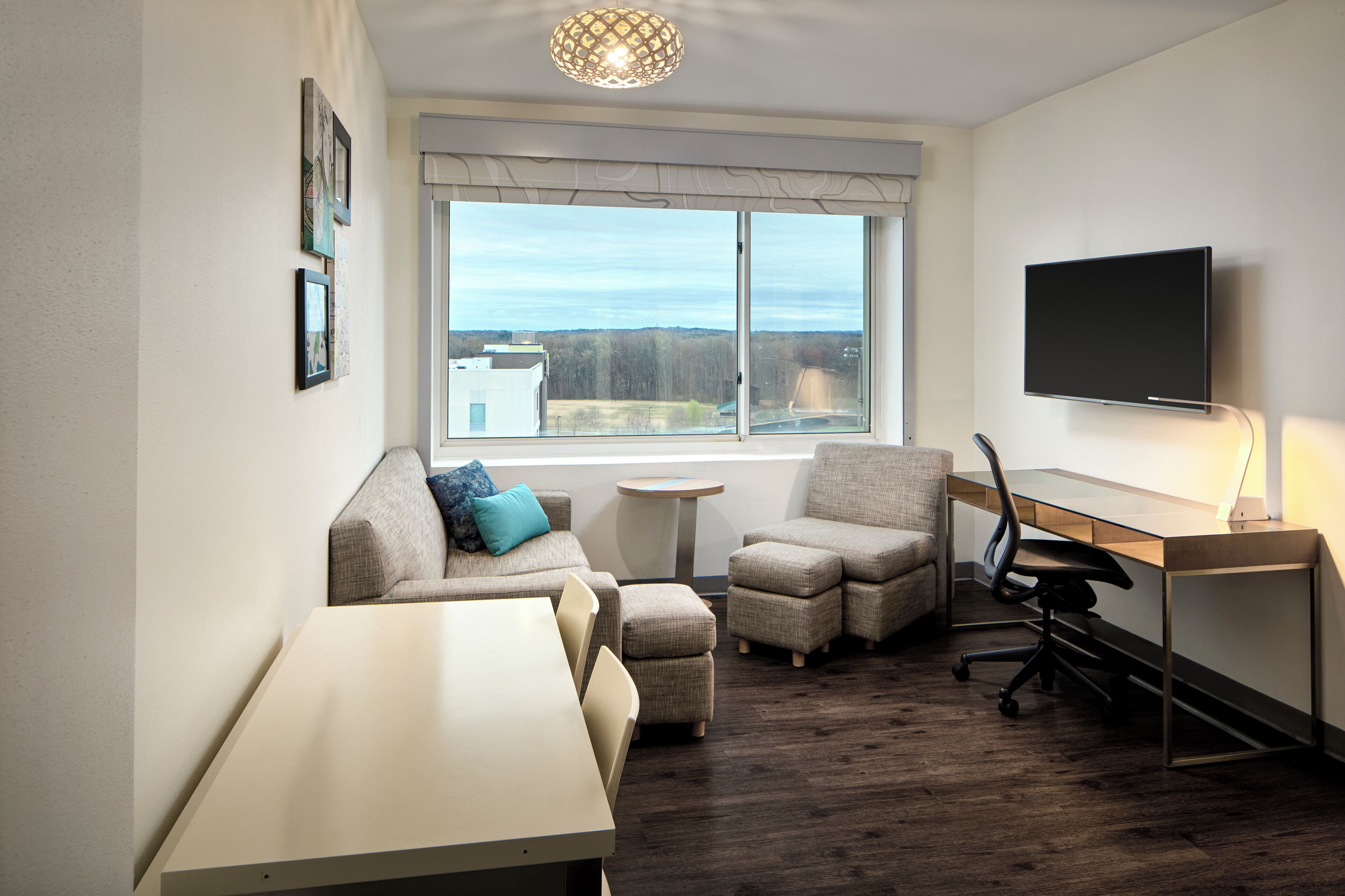 Une chambre moderne équipée d’un bureau, de deux chaises, d’un canapé, d’une télévision et d’une fenêtre donnant sur un paysage agréable.