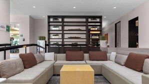 A modern hotel lobby with a sectional sofa, a wooden coffee table, and a shelving unit with plants. - Element by Marriott Arundel Mills BWI Airport (Hanover)