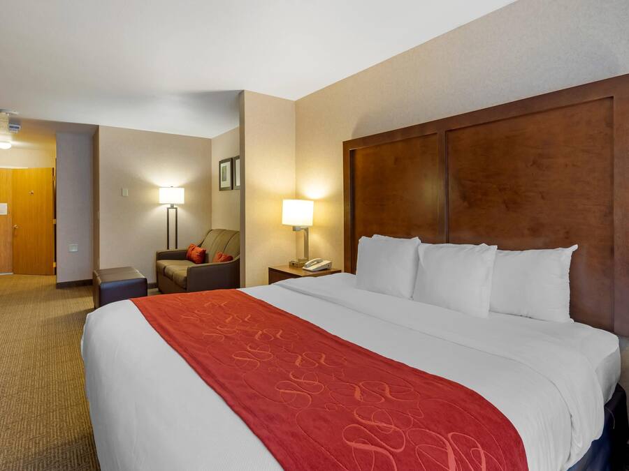 A hotel room with a large bed, a nightstand with a lamp, a chair, and a wooden door.