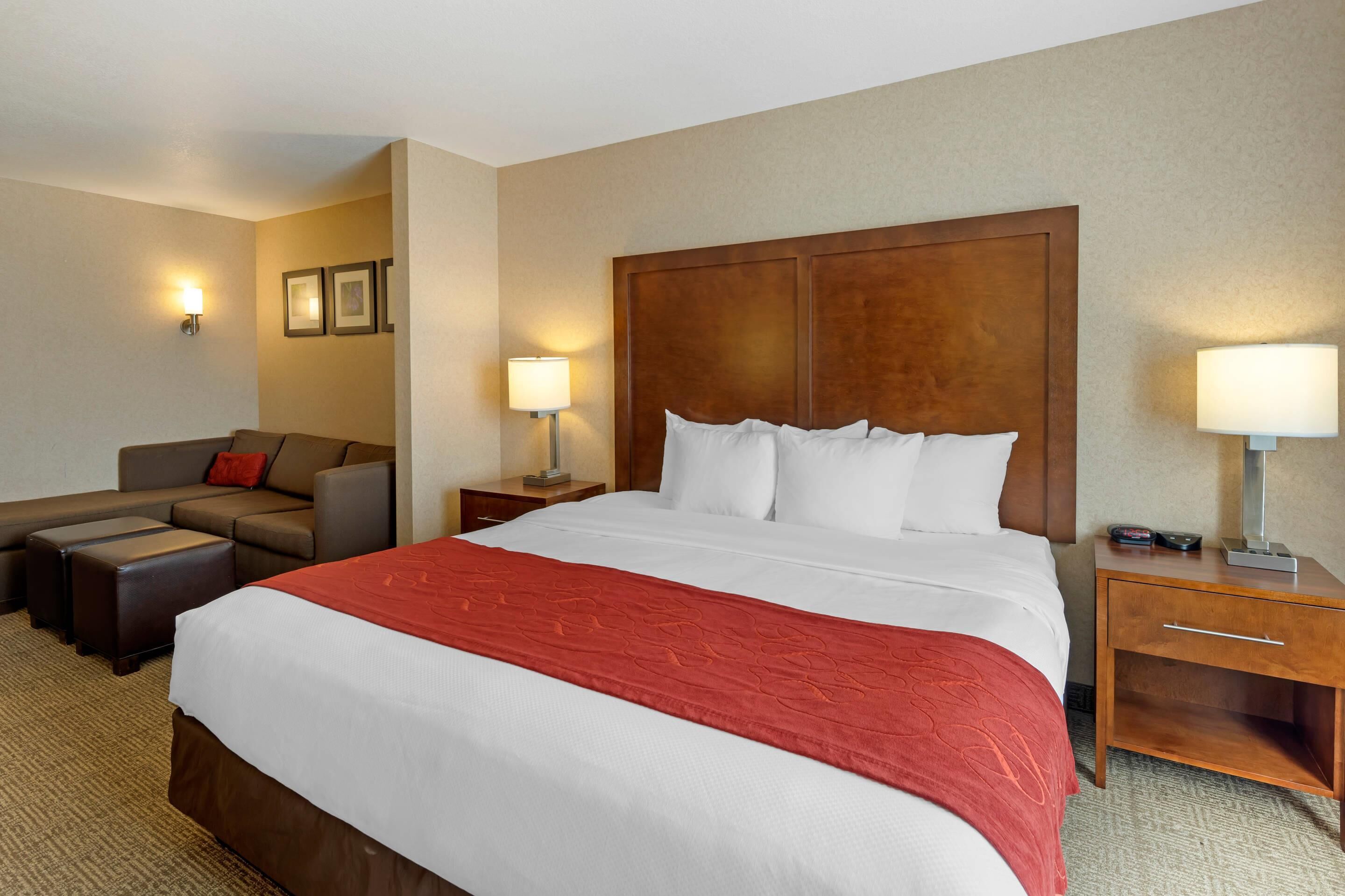 Una habitación de hotel con una cama grande, un sofá, una mesita de noche y una lámpara.