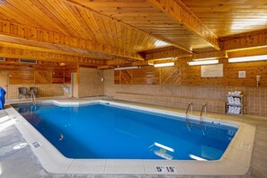 Une piscine intérieure avec des poutres en bois au plafond, des murs carrelés et un panneau indiquant une profondeur de 5 pieds et 15 pouces.