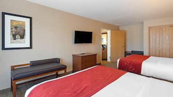 A hotel room with two beds, a bench, a TV, a dresser, and a door leading to another room.