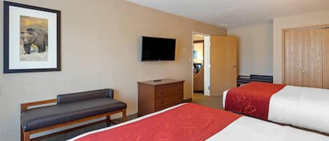 A hotel room with two beds, a bench, a TV, a dresser, and a door leading to another room.