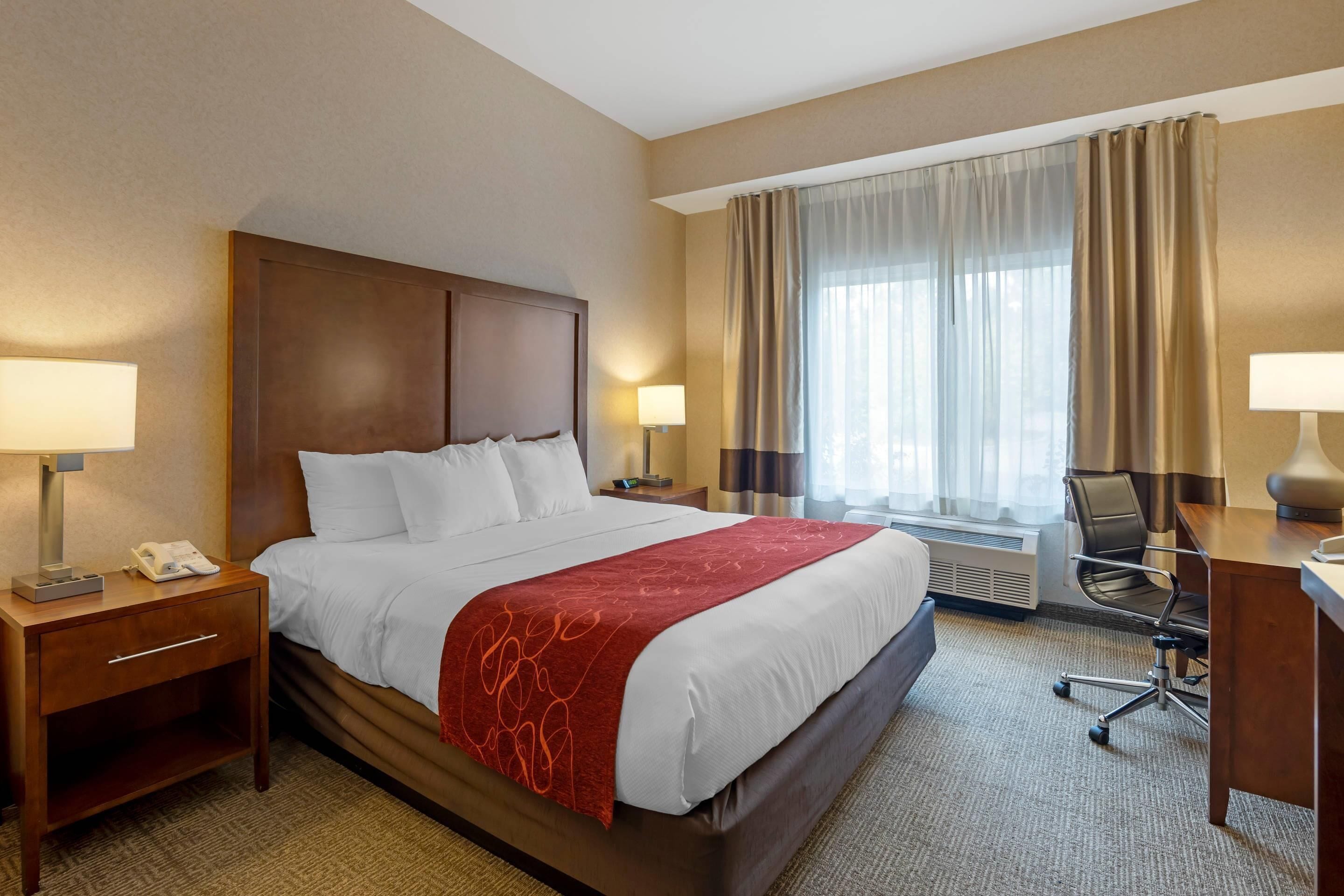 A hotel room with a large bed, two bedside tables with lamps, a desk, and a chair.