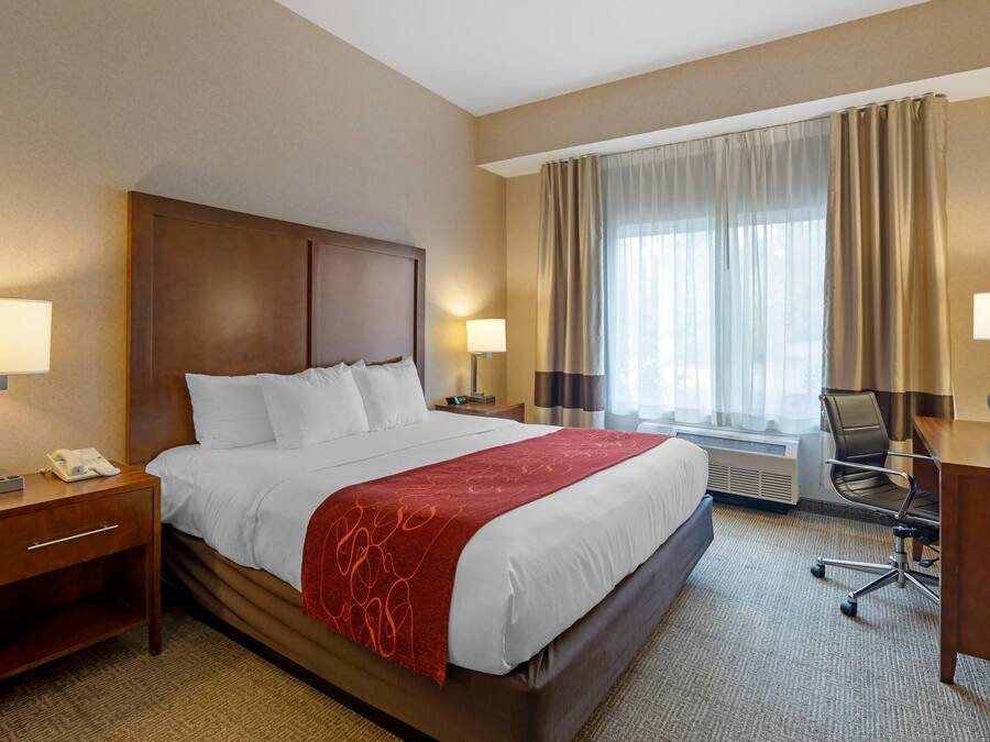 A hotel room with a large bed, two bedside tables with lamps, a desk, and a chair.