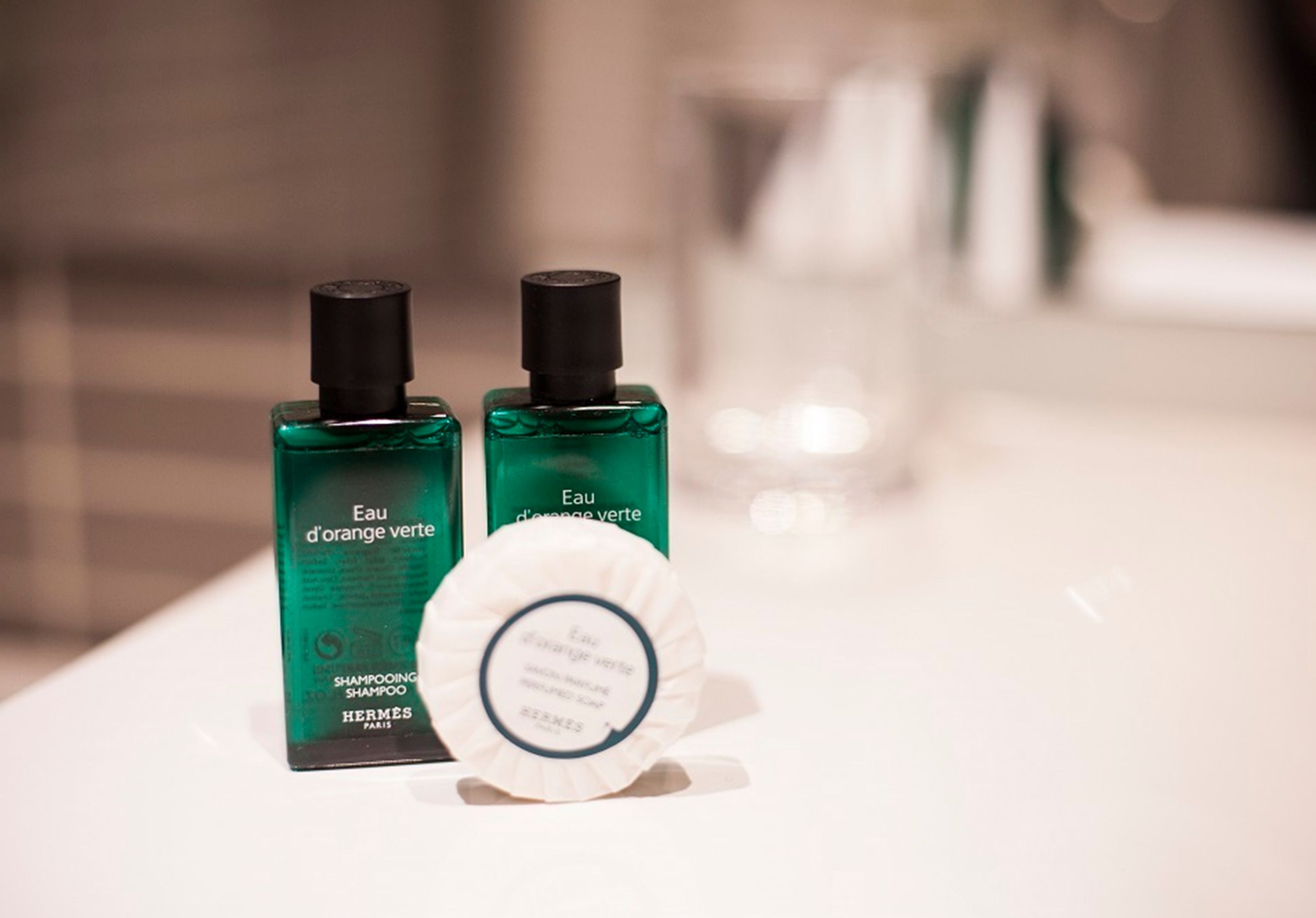 Dos botellas de champú verde y una pastilla de jabón blanco sobre una encimera de baño.