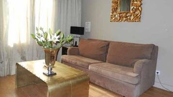 Een woonkamer met een bruine bank, een glazen salontafel en een decoratieve vaas met groene planten.