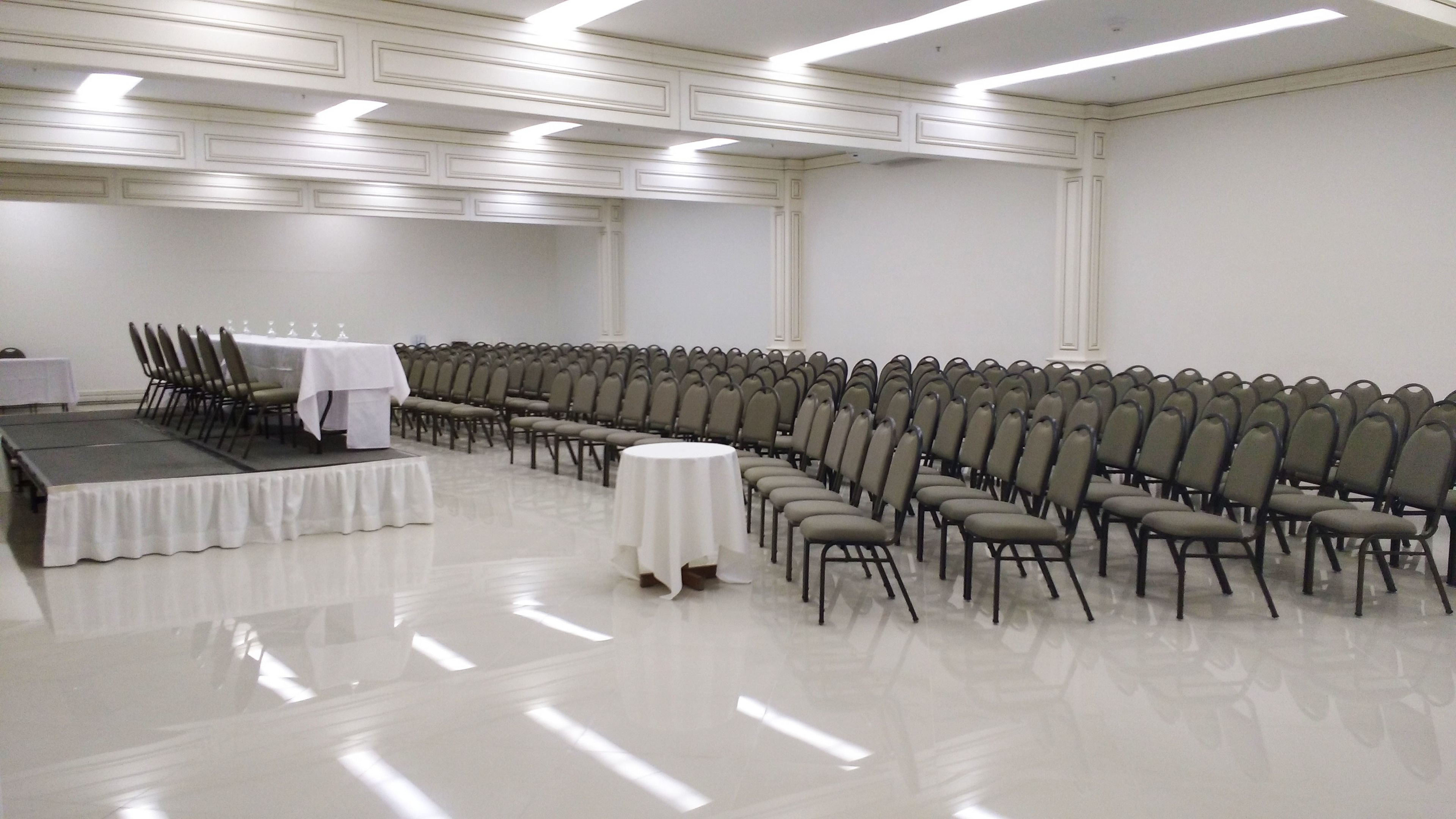 A conference room with rows of chairs, a stage with a table, and a white table in the center.