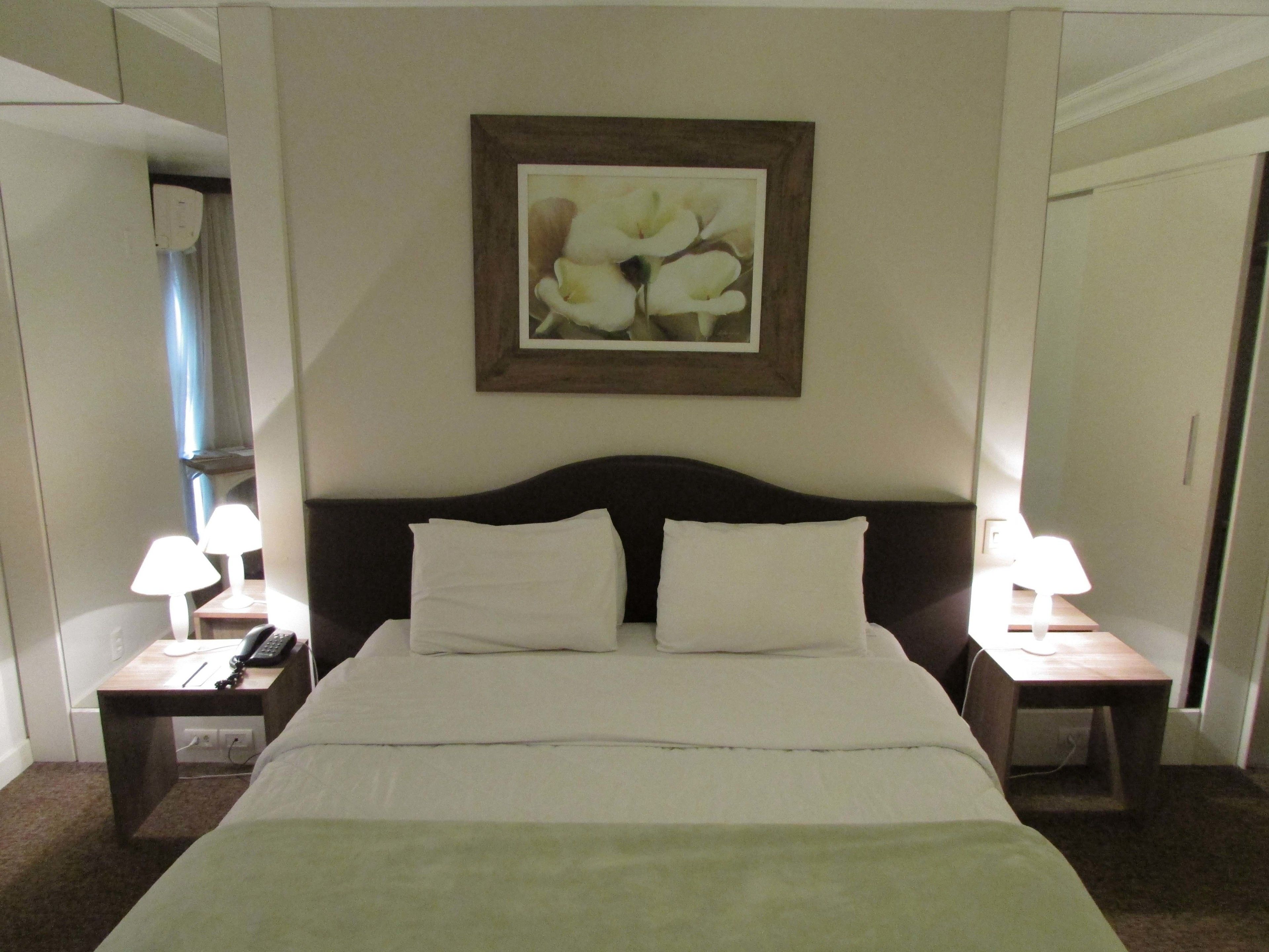 A hotel room with a large bed, two bedside tables with lamps, a telephone, and a framed picture on the wall.