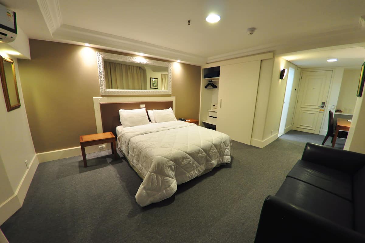 A hotel room with a bed, bedside table, and a mirror. There is a door leading to a bathroom and a hallway.