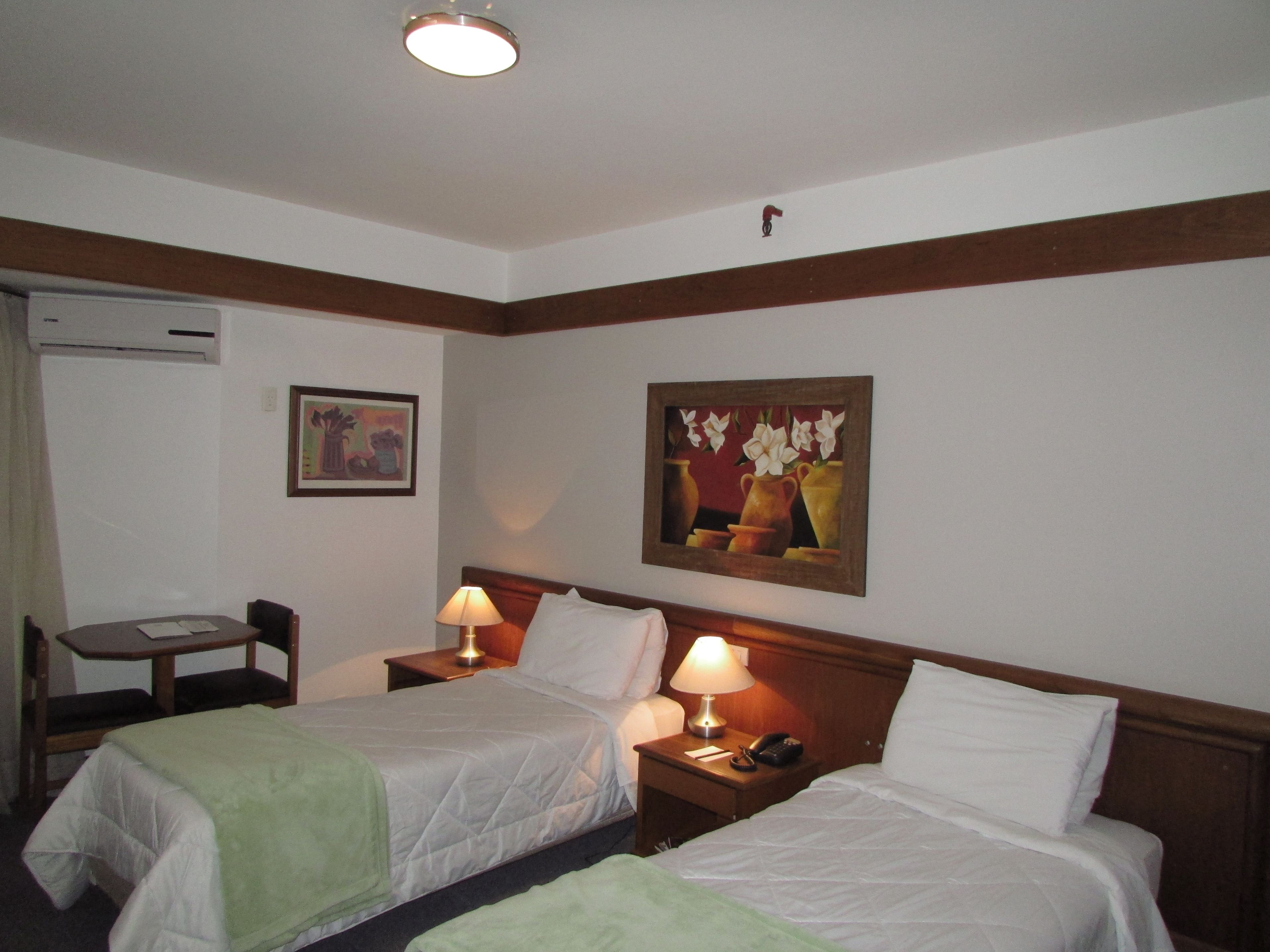 Une chambre d’hôtel avec deux lits, un bureau, une chaise, une lampe et un tableau au mur.