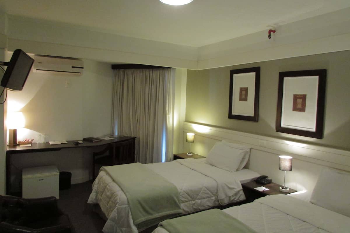 A hotel room with two beds, a desk, a chair, a TV, and a bedside table with a lamp.