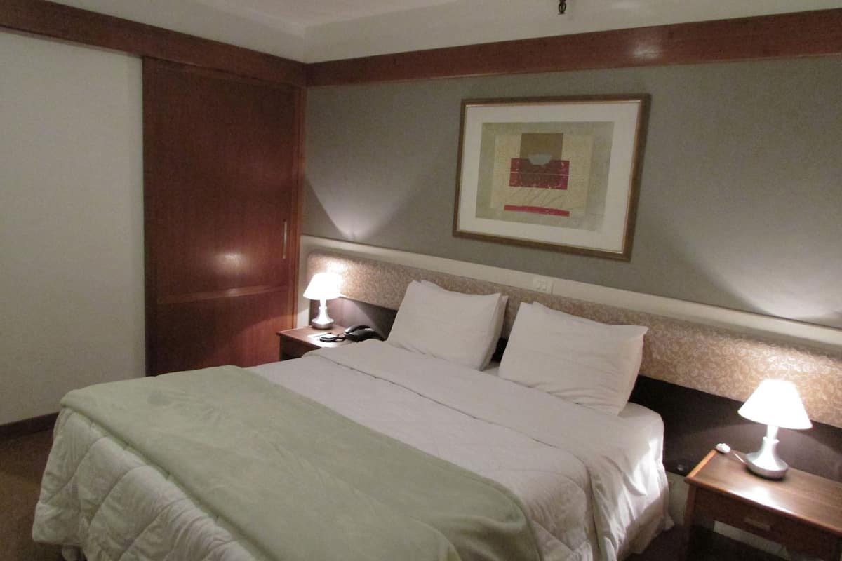 A hotel room with a bed, two bedside tables, a lamp, a phone, and a framed picture on the wall.