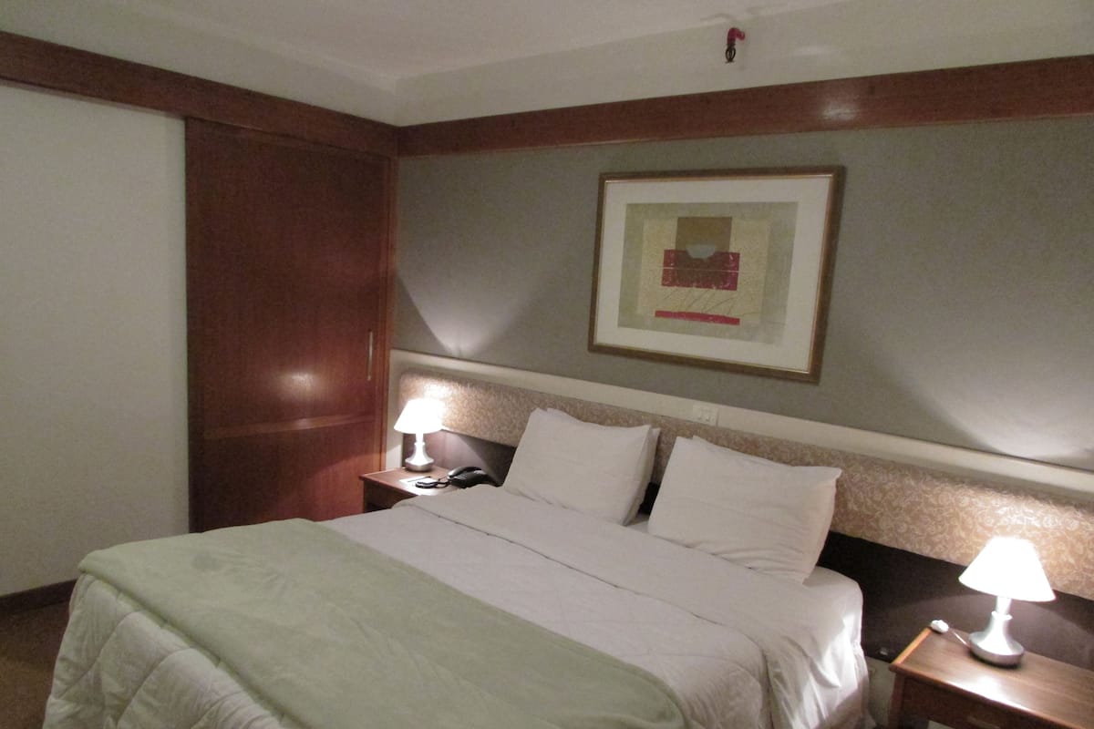 A hotel room with a large bed, a bedside table with a lamp, a phone, and a framed picture on the wall.