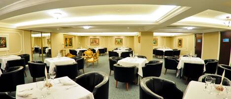 A banquet hall with multiple round tables, black chairs, and white tablecloths.