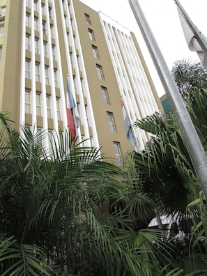 A tall building with multiple windows and balconies, surrounded by lush green palm trees.