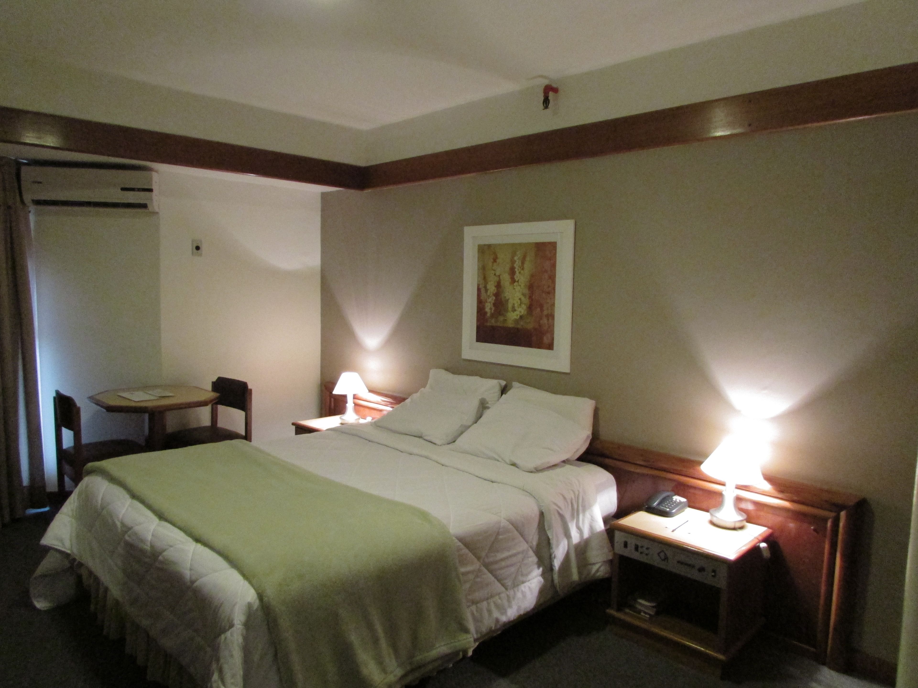 Una habitación de hotel con una cama, lámparas de noche, un escritorio y una silla.