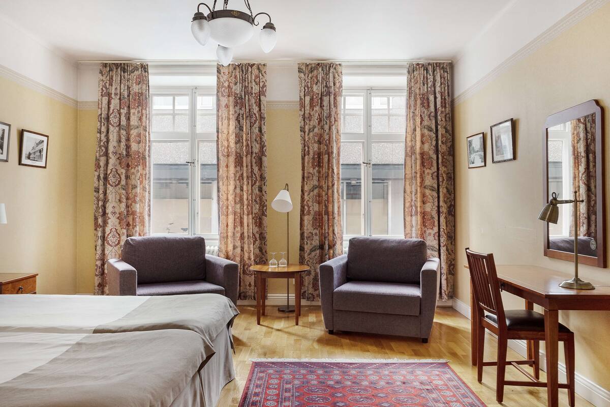 A hotel room with two sofas, a small table with glasses, a desk with a chair, and a large mirror.
