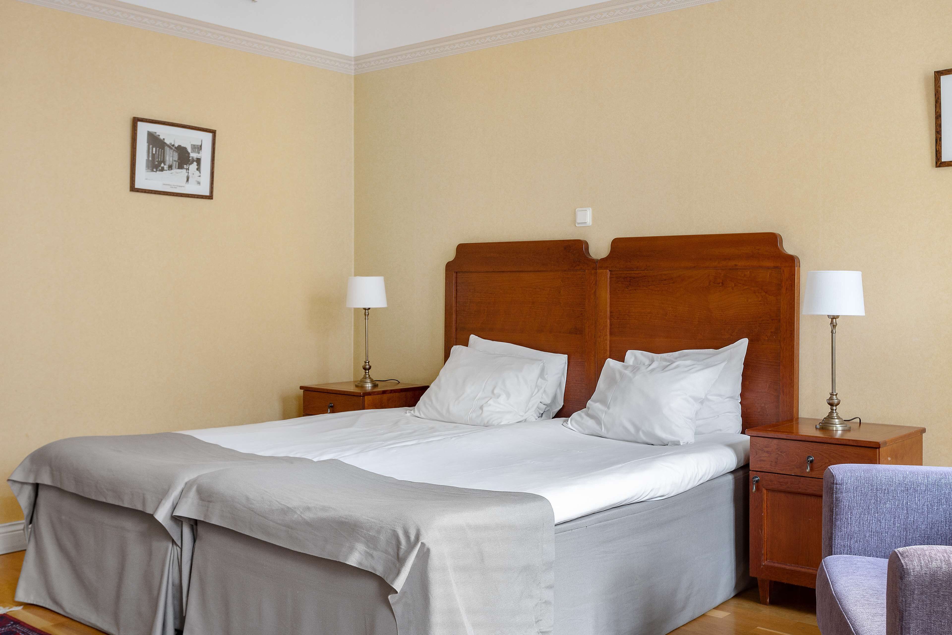 A neatly made bed with white linens, a wooden headboard, and two bedside tables with lamps.