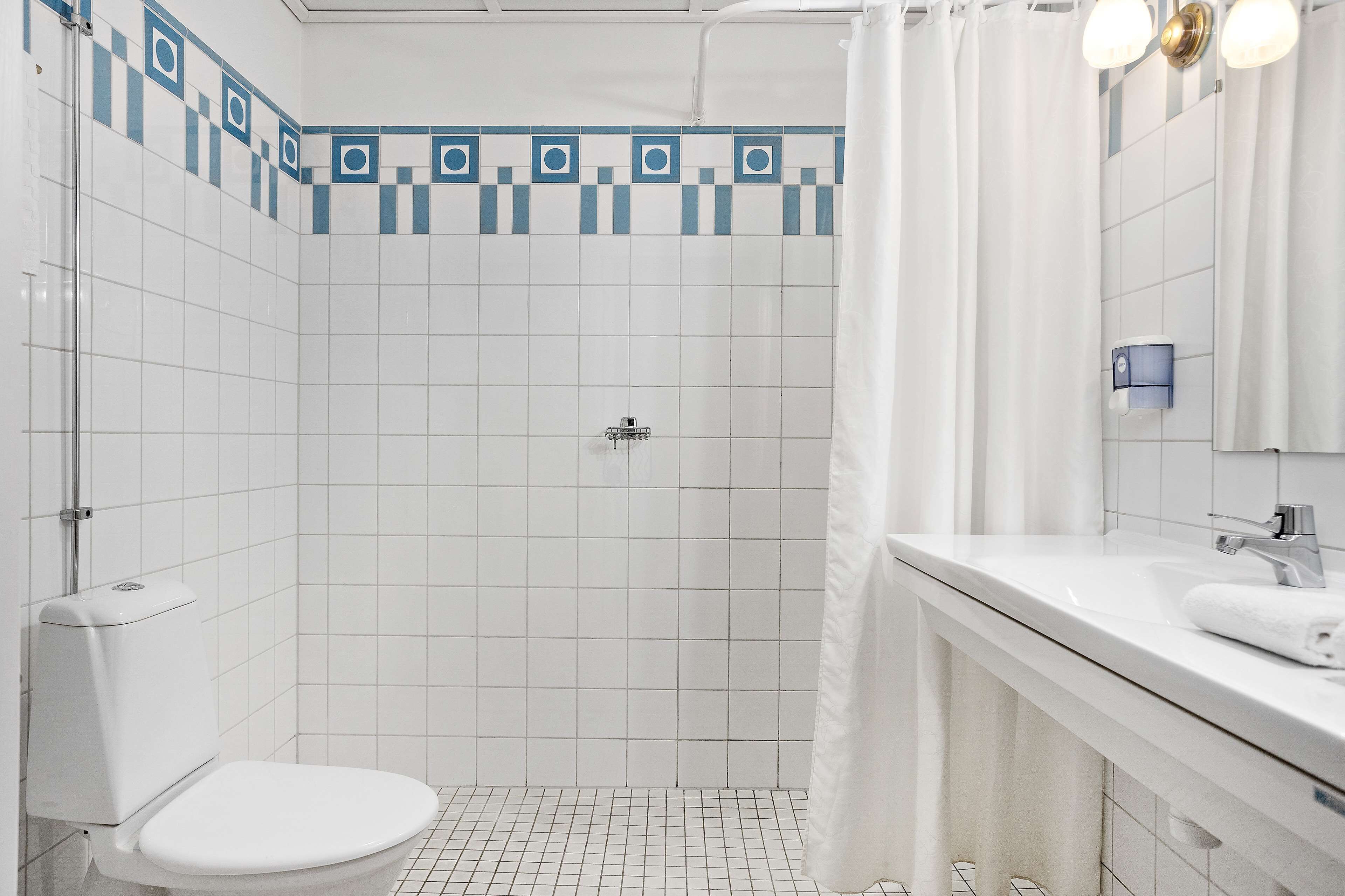 Et badeværelse med toilet, bruseniche og et spejl ved håndvasken.