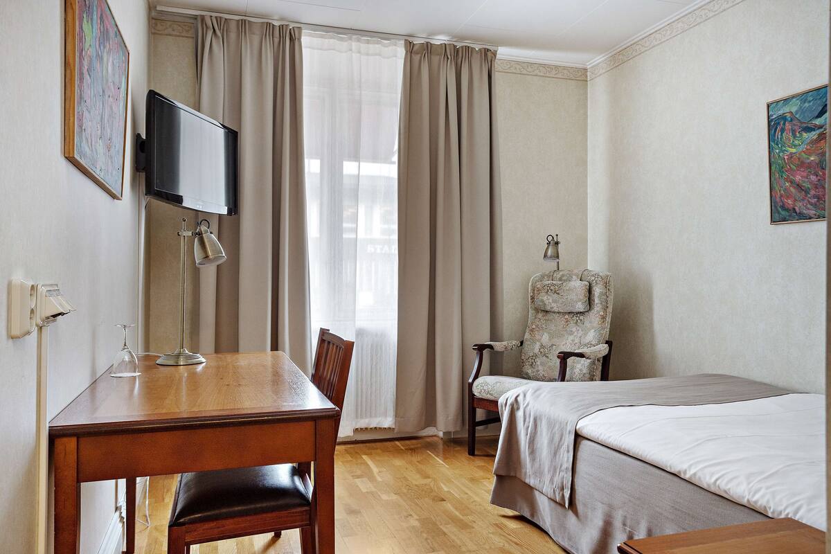 A hotel room with a wooden desk, a bed, a chair, and a television on the wall.