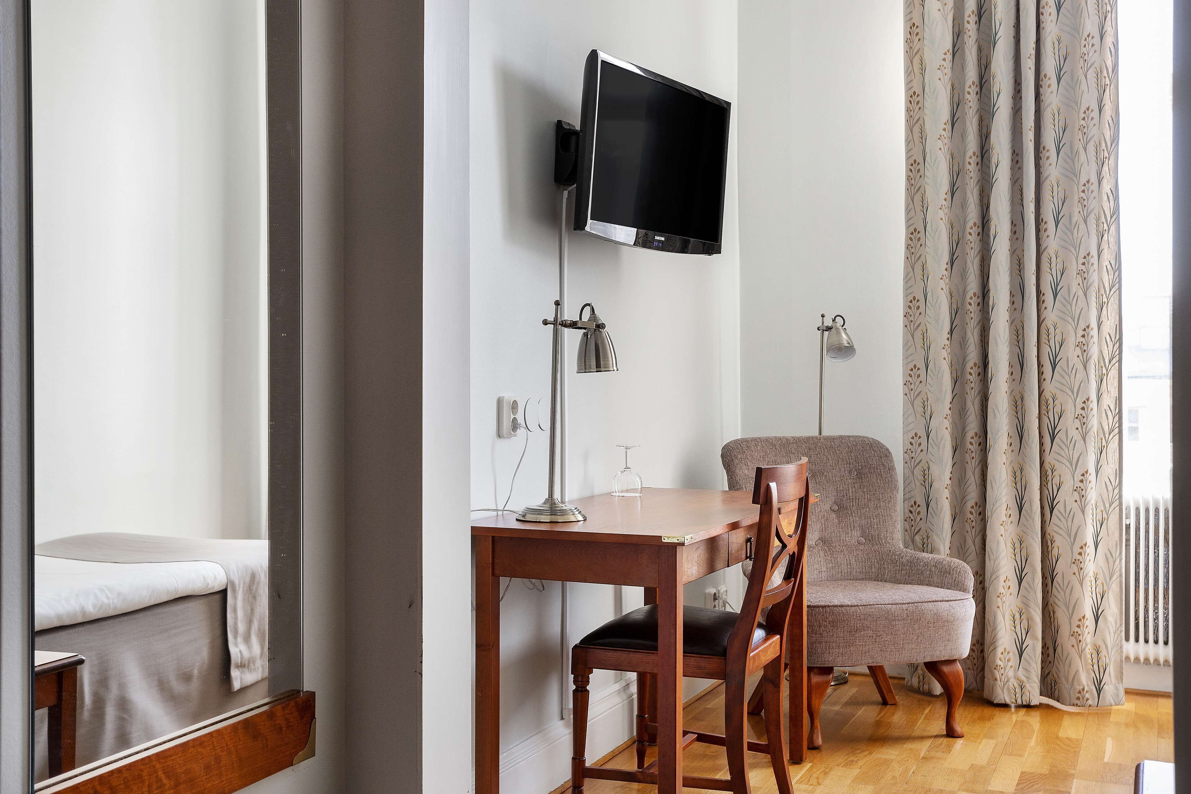 A modern room with a flat-screen TV mounted on the wall, a wooden table with a chair, and a patterned curtain.